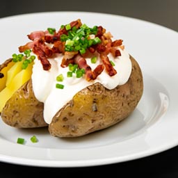 A baked russet potato topped with sour cream, cheddar cheese, bacon bits, and chives.